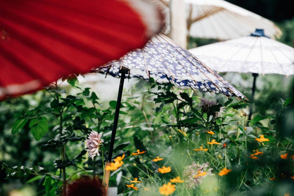 Two hands adjusting a wooden garden parasol beside blooming lavender and wicker chairs