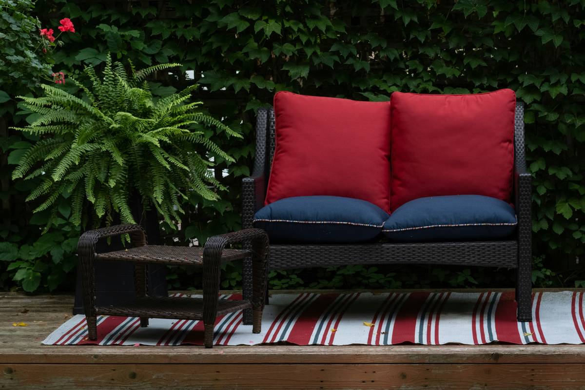 A weathered patio chair with a faded garden seat back cushion showing signs of sun damage but still providing comfortable support