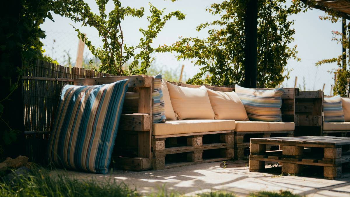 Stack of vibrant garden seat cushions on a weathered teak bench beside a garden parasol